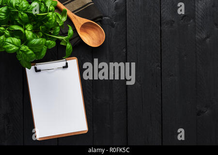 Vista superiore della pianta di basilico in una pentola con del cartone appunti per i menu o ricette su tavoli in legno nero con copia spazio. Di foglie di basilico fresco. Backgro alimentare Foto Stock