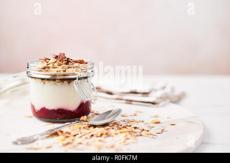 Una sana prima colazione. Un vasetto di yogurt sano con salsa di fragole, avena e cioccolato su marmo bianco piatto su sfondo rosa con copia spazio. Foto Stock