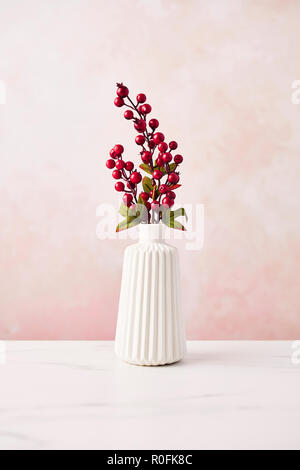 Artificiale di decorazione di interni. Rametto con bacche nel vaso su bianco tavola di marmo rosa su sfondo a parete. Copia dello spazio. Foto Stock