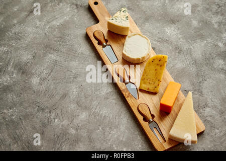 Assortimento di vari tipi di formaggi serviti sulla tavola di legno con forcella e i coltelli Foto Stock