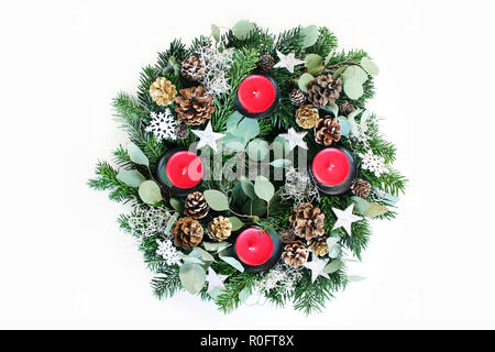 Natale corona di Avvento isolato sul tavolo bianco sullo sfondo. Decorata da evergreen Abete rami, foglie di eucalipto, fiocchi di neve, dorata e naturale pigne e candele rosse. Appartamento laico, vista dall'alto. Foto Stock