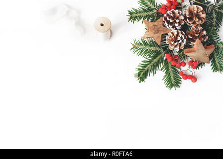 Christmas Festive composizione in stile. Banner decorativi. Coni di pino, abete rami, rosso rowan bacche, stelle di legno e seta nastro bianco su sfondo tabella. Lo spazio negativo. Appartamento laico, vista dall'alto. Foto Stock