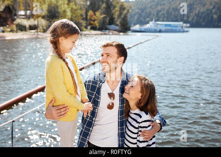 La famiglia felice di trascorrere del tempo insieme al di fuori del vicino lago. I genitori a giocare con la figlia abbracciando e divertirsi Foto Stock