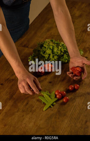 Lo chef con pomodorini, fagiolini, lattuga e peperoni in mano sul rustico di legno con luce fioca. Foto Stock