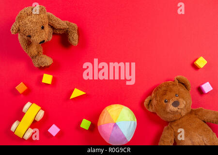 Baby giocattoli per bambini sfondo. Orsacchiotto di peluche, auto in legno, mattoni colorati su sfondo rosso Foto Stock