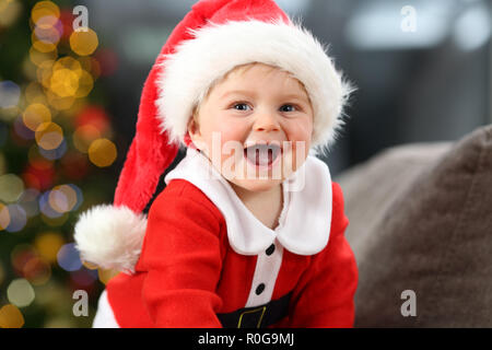 Kid indossa santa claus costume guardando a voi su un lettino a casa nel natale Foto Stock