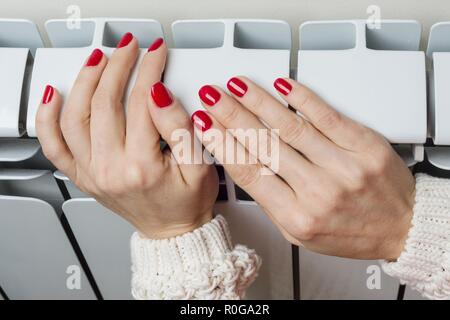 Riscaldamento radiatore bianco nell'appartamento, femmina mano sul radiatore. Foto Stock