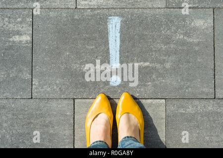I piedi femminili con punto esclamativo, simbolo di attenzione tracciata sull'asfalto. Foto Stock