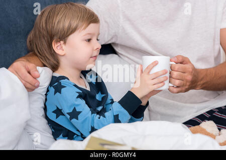 Ritagliato colpo di padre dando tazza di una bevanda calda al suo figlio nel letto Foto Stock
