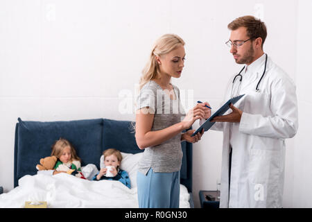 Pediatra dando appunti per la madre dei bambini malati che giace nel letto sullo sfondo di firmare documenti Foto Stock