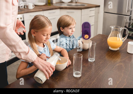 Ritagliato colpo di madre versando il latte in cereali per gli adorabili bambini piccoli durante la prima colazione Foto Stock