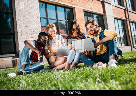 Interracial gruppo di studenti con laptop e notebook Studio sul prato verde insieme Foto Stock