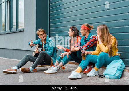 Hipsters bere birra insieme sulla strada, mentre l'uomo suonare la chitarra acustica Foto Stock