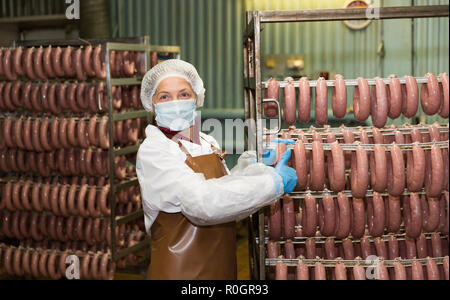 Lavoratore di sesso femminile che trasportano materie salsicce in rack in stanza di deposito alla trasformazione della carne factory Foto Stock