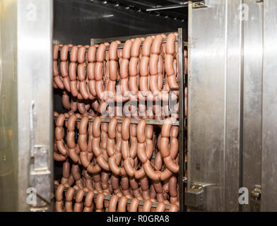 Cuocere le salsicce appese in rack in forno alla fabbrica di salumi Foto Stock