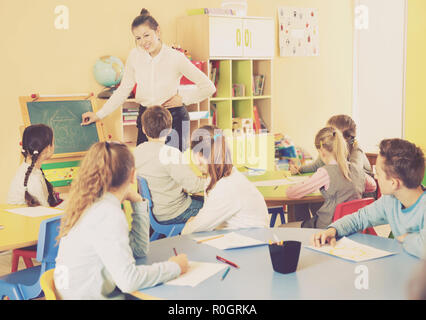 Giovani insegnanti di sesso femminile in piedi alla lavagna in aula, conducendo la lezione con i bambini Foto Stock