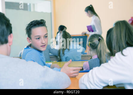 Felice di chattering alunni seduti sui banchi torna alla lezione di scuola elementare Foto Stock