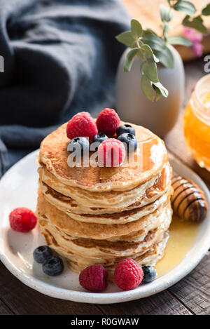 Oat pancake con mirtilli, lamponi e miele per la colazione sulla piastra bianca sul tavolo di legno. Messa a fuoco selettiva Foto Stock