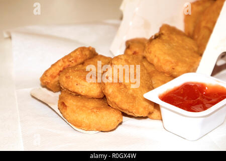 Pila di fritto di pollo croccante pepite fuoriuscita da una scatola di carta con ketchup Foto Stock