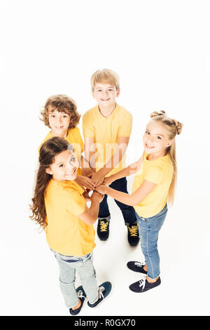 Elevato angolo di vista adorabili bambini felici mani di impilamento e sorridente in telecamera isolato su bianco Foto Stock