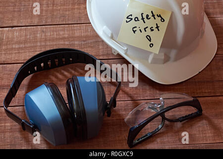 La sicurezza prima di tutto nota uno giallo pezzo di carta bloccata su sfondo di legno con una gamma completa di attrezzature per la protezione personale: casco, occhiali safet e orecchio p Foto Stock