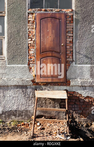 Ingresso del distrutto edificio, porta di legno, Scale di metallo, finestra con i vecchi telai di legno, rosso mattone e cemento grigio. Concetto tessiturali sfondo Foto Stock