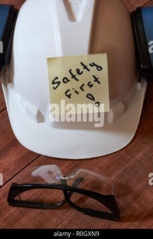 La sicurezza prima di tutto nota uno giallo pezzo di carta bloccata su sfondo di legno con una gamma completa di attrezzature per la protezione personale: casco, occhiali safet e orecchio p Foto Stock