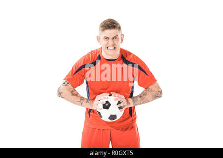 Angry Young soccer giocatore in possesso palla e guardando la telecamera isolato su bianco Foto Stock