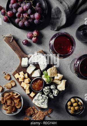 Il piatto di formaggi serviti con un bicchiere di vino rosso, olive, uva, marmellata e bocconcini di pane sul marmo grigio Sfondo. Vista dall'alto. Foto Stock