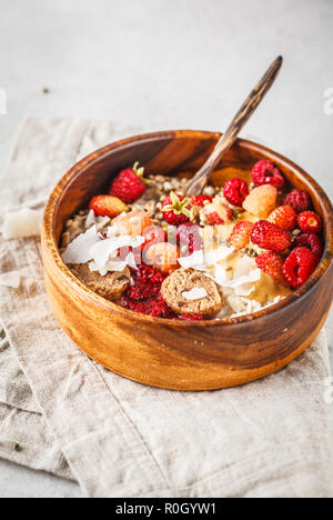 Vegano Trendy ciotola di porridge di avena con frutti di bosco, raw vegan palle e burro di arachidi nella ciotola di legno. Foto Stock