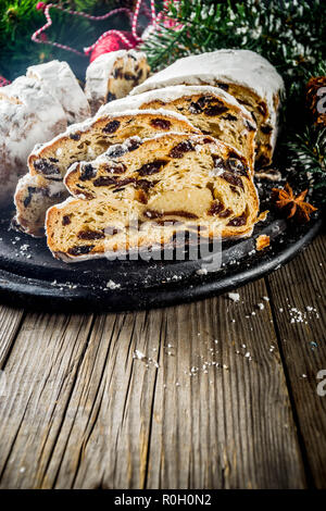 Europeo tradizionale pasticceria di Natale, fragrante cotto domestico stollen con spezie e frutta secca. Affettare sul tavolo di legno con il natale a rami di alberi e de Foto Stock