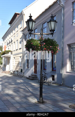 Old-style street lanterna con due lampade e vasi sospesi con fiori di colore rosso su strada Foto Stock