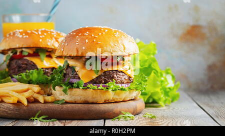 Due freschi fatti in casa hamburger con patatine fritte e succo di arancia su di un tavolo di legno. Con copia spazio. Foto Stock