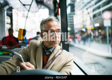 Imprenditore maturo con lo smartphone in viaggio in autobus in città. Foto Stock