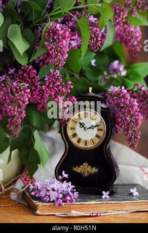 Natura morta con fiori lilla e vecchio orologio sul tavolo di legno Foto Stock