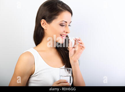 Sorridenti donna positiva di mangiare la pillola e tenendo il bicchiere di acqua nella mano su sfondo bianco. Primo piano vista di profilo verticale. Foto Stock