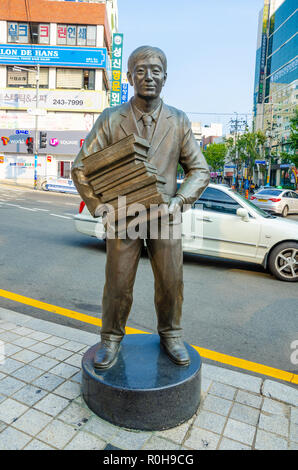 Scultura in bronzo raffiguranti la figura di un uomo che porta una pila di libri sorge su un angolo di strada vicino a Bosu Dong Prenota vicolo in Busan,, la Corea del Sud. Foto Stock