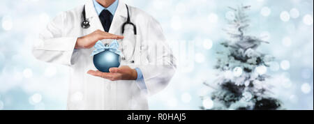 Auguri di Buon Natale dal medico,, auguri concetto, mani con palla di Natale sulla luce sfocata e albero, gift card banner modello web con spazio di copia Foto Stock