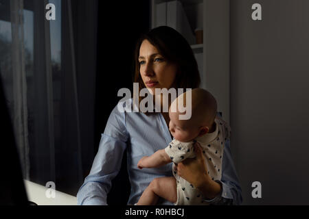 Imprenditrici occupato a lavorare in un ufficio con un bambino sulle mani. Lavora fino a tardi concetto. Foto Stock