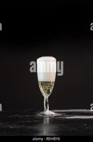 Golden champagne versata da una bottiglia in un bicchiere, visibili gocce, bolle e un tocco Foto Stock
