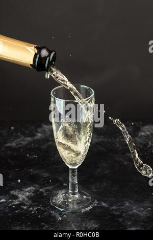 Golden champagne versata da una bottiglia in un bicchiere, visibili gocce, bolle e un tocco Foto Stock