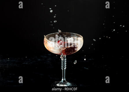 Bicchiere di rosso di cocktail con frutti rossi su sfondo nero, visibili gli schizzi, gocce e la circolazione del liquido Foto Stock