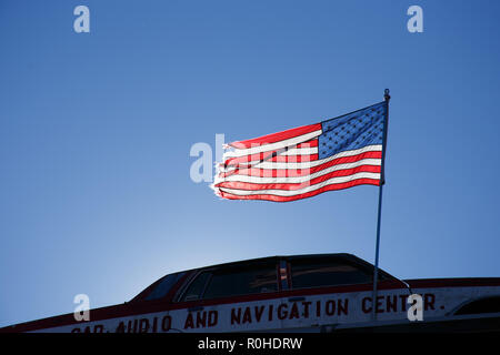 Usurati bandiera americana onde del vento sulla cima di una vecchia auto che si trova sul tetto di un negozio di riparazioni auto. Foto Stock