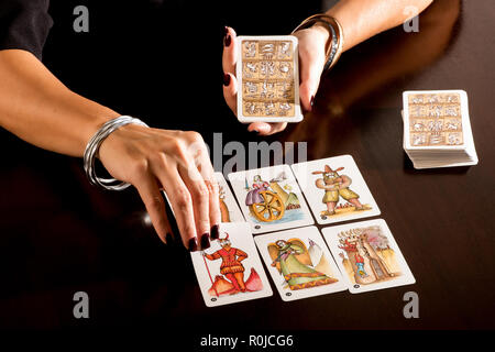 Indovino la lettura di un mazzo di simbolico pittorica Tarocchi in un close up sulle sue mani la loro posa in opera su di un tavolo per fare la sua profezia Foto Stock