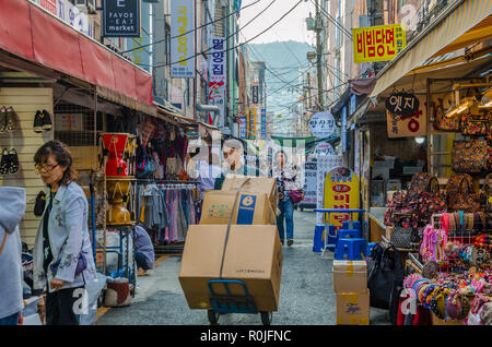 Strada trafficata scena di mercato in Busan, Corea del Sud. Street è pieno f people shopping come un uomo spinge un carrello caricato con scatole di cartone . Foto Stock