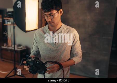 Maschio asiatici fotografo di controllare e regolare la sua reflex digitale impostazione in studio. Fotografo per configurare il suo fotocamera prima le riprese in studio. Foto Stock