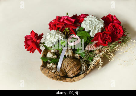 Bouquet di rose rosse, bianche ortensie, decorate con rami di eucalipto con conchiglie in un cesto di paglia sulla luce di un tavolo di legno Foto Stock