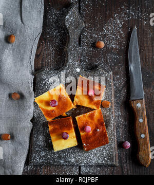 Quattro quadrati di fette di formaggio e torta di zucca su una tavola di legno, dessert è spolverato con zucchero a velo, vista dall'alto Foto Stock