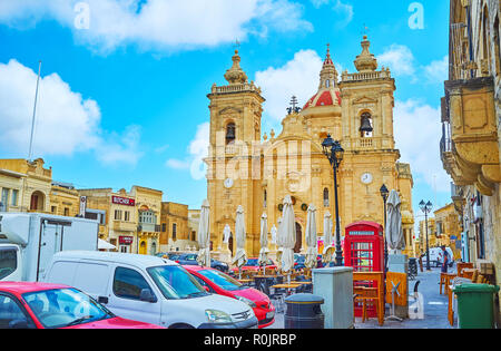 XAGHRA, Malta - 15 giugno 2018: la vista sulla Basilica della Natività dalla trafficata piazza con molte automobili parcheggiate e caffè all'aperto, il 15 giugno a Xaghra. Foto Stock