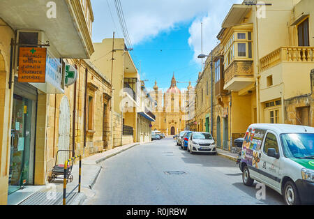 XAGHRA, Malta - 15 giugno 2018: a piedi la strada stretta con una vista sulla grande Basilica della Natività sulla distanza, il 15 giugno a Xaghra. Foto Stock